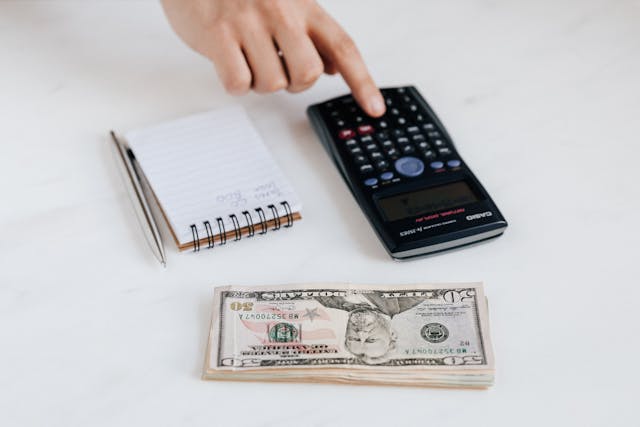 a stack of cash next to a calculator and a notebook