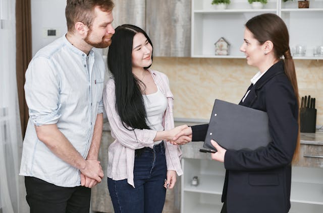 a couple in a kitchen shaking the hand of a woman in a black suit