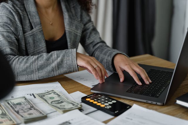 woman in a suit working on a laptop with a calculator next to her